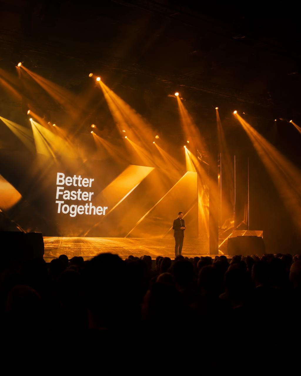 Corporate keynote stage with amber light beams and a large LED wall